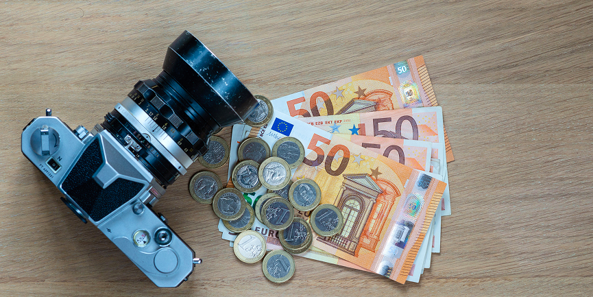 Kamera liegt auf Euro-Scheinen und -Münzen, Symbol für Einnahmen und Geschäftsmodelle in der Fotografie.